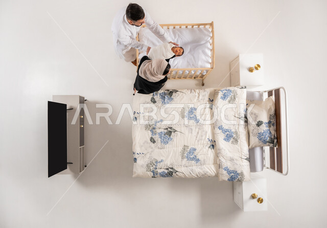 قضاء الوقت باللعب مع الاولاد، مداعبه الأبناء بحب وحنان، العناية بالاطفال حديثي الولاده، بورتريه علوي عامودي لاب وام عربيان خليجيان عمانيان يحملان طفلهما الرضيع بحرص واهتمام، مفهوم الاسرة وتحمل المسؤولية، عائلة سعودية تقوم برعايه ابنهم، خلفية بيضاء