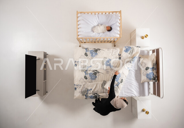 اداء الواجبات وتنظيم المنزل، مفهوم الاسرة وتحمل المسؤولية، العناية بالاطفال حديثي الولاده، دور الأهل في حياه الأبناء، امرأة سعودية تقوم بانجاز المهام المنزلية، بورتريه علوي عامودي لام عربيه خليجيه عمانية ترتيب سريرها، خلفيه بيضاء