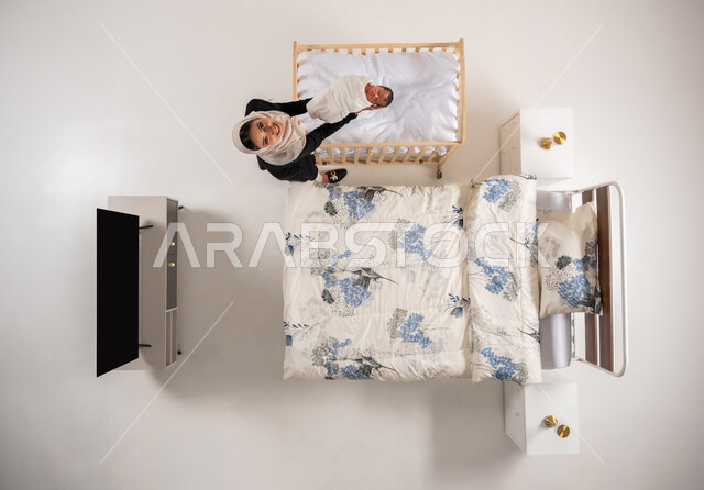 العناية بالاطفال حديثي الولاده، تقديم مشاعر الحب والحنان للاولاد، دور الأهل في حياه الأبناء، امرأة سعودية تقوم بملاطفة ولدها، بورتريه علوي عامودي لام عربيه خليجيه عمانية تحمل بيدها طفلها، مفهوم الاسرة وتحمل المسؤولية، خلفيه بيضاء