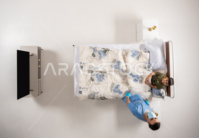 الالتزام بالاجراءات الوقائية ضد فايروس كورونا، بورتريه علوي عامودي لممرض عربي خليجي عماني يرتدي اليونيفورم والكمامة الطبية يقوم بتقديم الرعاية الطبية لولد مريض مستلقي على سريره، مفهوم الطب والرعاية الصحية، رجل سعودي يقوم بتقديم العلاج لصبي صغير، خلفيه بيضاء