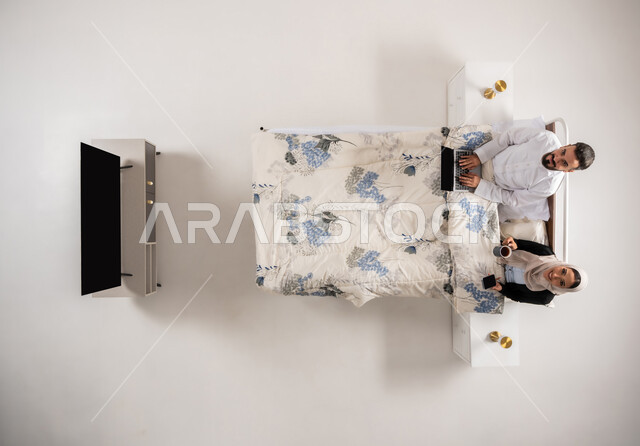 النظر الى الكاميرا بتعابير السرور، سيدة عمانية تمسك بيدها الهاتف المحمول تقوم بتصفح مواقع التواصل الاجتماعي، بورتريه عامودي علوي لإمرأه وشاب عربيان سعوديان خليجيان يجلسان على سرير مريح يستخدمان الأجهزة التقنية، رجل عماني يقوم بإنجاز مهام العمل، خلفية بيضاء