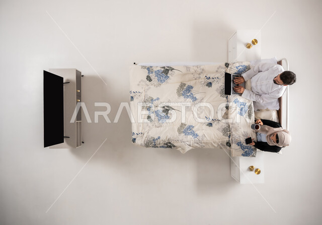 Omani man doing work tasks with expressions of concentration, Omani woman holding mobile phone in hand drinking hot drinks, vertical top portrait of Saudi Arabian Gulf woman and young man sitting on comfortable bed using modern technology devices, white background