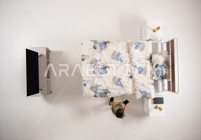 تصفح مواقع التواصل الاجتماعي، صبي عماني يمسك بيده جهاز الهاتف المحمول, استعمال الأجهزة التكنولوجية الحديثة والمتطورة, بورتريه علوي عامودي لولد عربي خليجي سعودي يقف امام السرير في غرفه النوم يقوم باستخدام الجوال, خلفية بيضاء