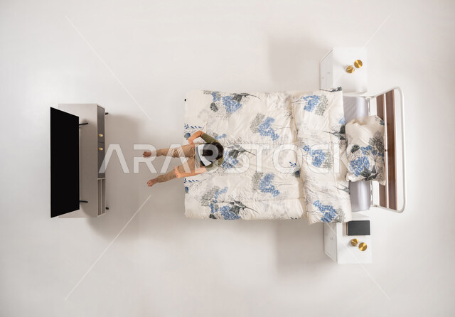 محاكاه العالم الخيالي، استخدام الأجهزة التكنولوجية الحديثة والمتطورة, بورتريه علوي عامودي لولد عربي خليجي سعودي يجلس على سريره في غرفه النوم بتعابير الاندماج, صبي عماني يرتدي نظارات الواقع الافتراضي يشاهد شيء ما, خلفية بيضاء