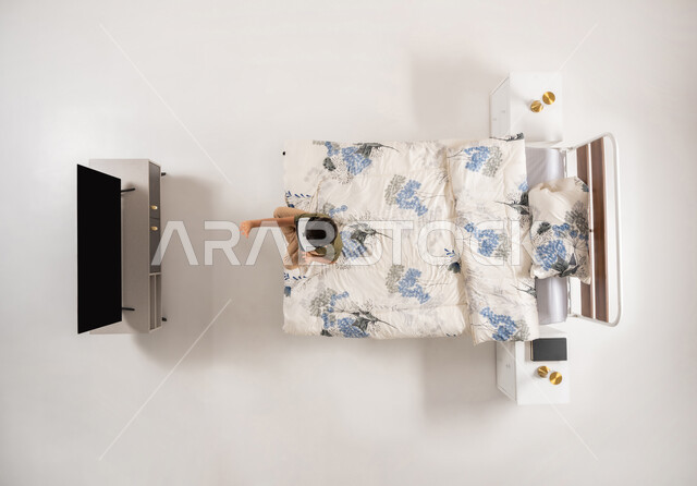 محاكاه العالم الخيالي، استخدام الأجهزة التكنولوجية الحديثة والمتطورة, بورتريه علوي عامودي لولد عربي خليجي سعودي يجلس على سريره في غرفه النوم بتعابير الاندماج, صبي عماني يرتدي نظارات الواقع الافتراضي يشاهد شيء ما, خلفية بيضاء