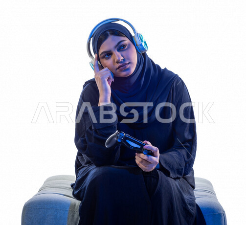 بورتريه مرأة عربية سعودية خليجية , تقوم  بإيماءات وجه تدل على التفكير والتخطيط ، ترتدي سماعة رأس و تمسك عصا التحكم و تلعب بألعاب الفيديو ، المتعة و التسلية بألعاب الفيديو  ، ألعاب البلايستيشن الترفيهية ، تقنيات و ألعاب ، خلفية بيضا