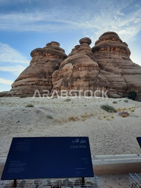 Rock formations in AlUla in the middle of the deserts of the Kingdom of Saudi Arabia, ancient historical landmarks in Madain Saleh, tourist places in desert areas, a blue metal sign for the Athlab Mountains in the desert, the growth of wild and thorny plants