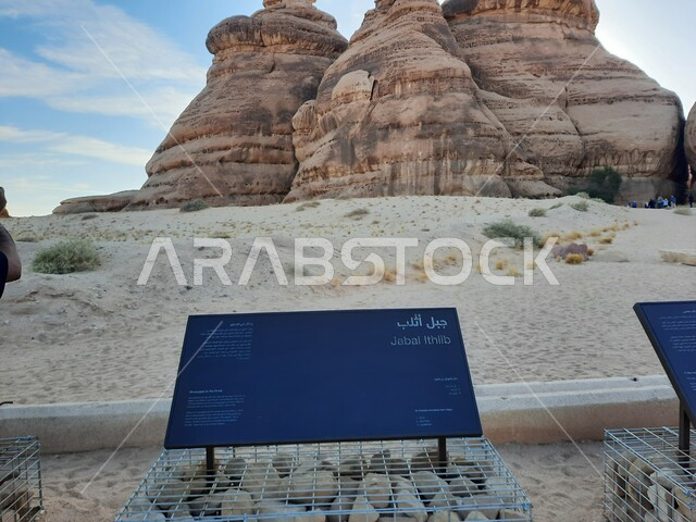 Rock formations in AlUla in the middle of the deserts of the Kingdom of Saudi Arabia, ancient historical landmarks in Madain Saleh, tourist places in desert areas, a blue metal sign for the Athlab Mountains in the desert, the growth of wild and thorny plants