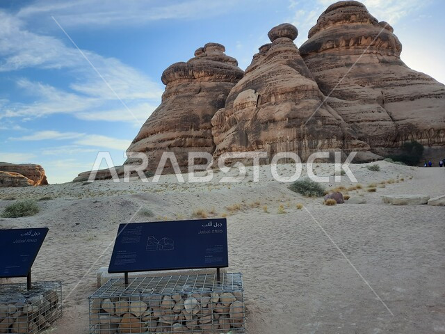 Rock formations in AlUla in the middle of the deserts of the Kingdom of Saudi Arabia, ancient historical landmarks in Madain Saleh, tourist places in desert areas, a blue metal sign for the Athlab Mountains in the desert, the growth of wild and thorny plants