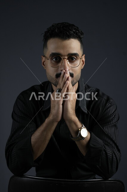 إيجاد حل لمشكلة ما، التأمل والتخطيط للمستقبل، بورتريه لشاب عربي خليجي سعودي يرتدي الزي الكاجوال يضع يده على ذقنه و ينظر إلى الكاميرا بإيماءات التفكير، التمعن والتركيز وشرود الذهن ، خلفية سوداء