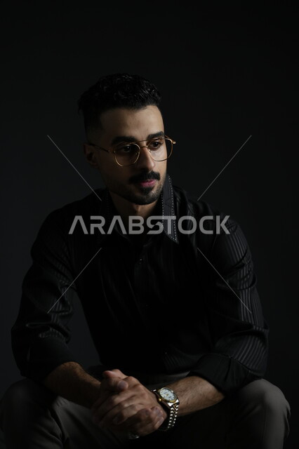 مفهوم الرجولة و الاهتمام بالمظهر الخارجي، بورتريه لشاب وسيم عربي خليجي سعودي يرتدي الزي الكاجوال ينظر إلى مكان ما بإيماءات الثقة بالنفس، الملامح العربية الاصيلة، خلفية سوداء