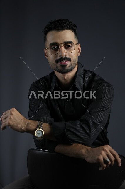 مفهوم الرجولة و الاهتمام بالمظهر الخارجي، بورتريه لشاب وسيم عربي خليجي سعودي يرتدي الزي الكاجوال ينظر إلى الكاميرا بإيماءات الثقة بالنفس، الملامح العربية الاصيلة، خلفية سوداء