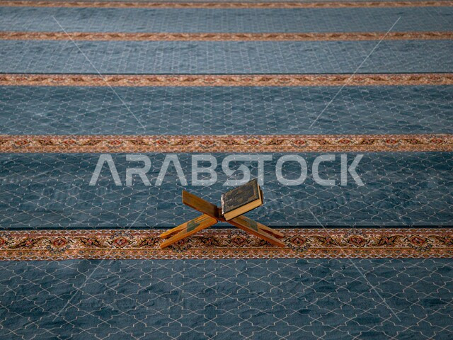 المصحف الشريف على حامل خشبي في المسجد، الصلاه والدعاء في المسجد، التقرب الى الله، قراءة وتلاوة القران، التعبد في بيوت الله، ذكر الله، مفهوم التمعن بآيات وسور القرآن الكريم، مكان مخصص للعبادة والطاعة، التلاوة والتحفيظ والتجويد