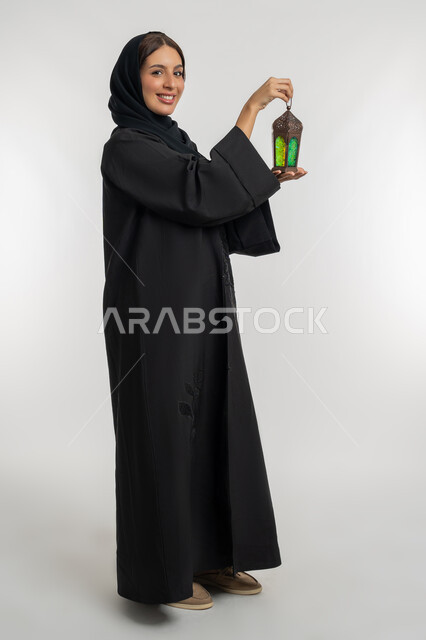 التحضير لاستقبال رمضان المبارك, البهجة بقدوم شهر الخير, بورتريه من الجانب لامرأة عربية خليجية إماراتية محجبة ترتدي العباءة السوداء تمسك بيدها فانوس معدني مزخرف, شابة سعودية تحتفل بالمناسبات الدينية الإسلامية, خلفية بيضاء