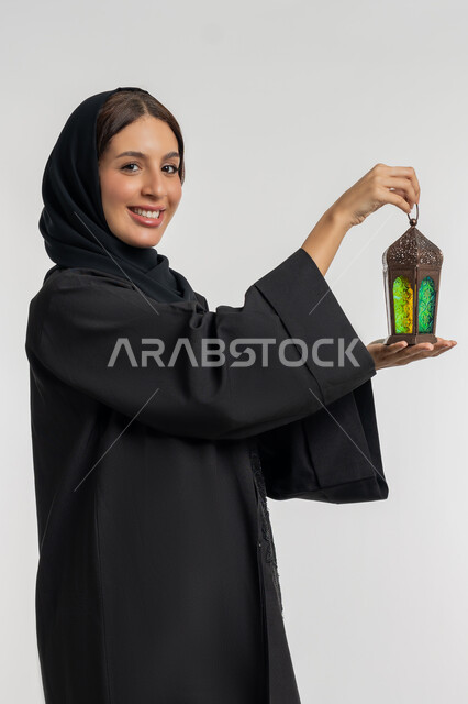التحضير لاستقبال رمضان المبارك, البهجة بقدوم شهر الخير, بورتريه من الجانب لامرأة عربية خليجية إماراتية محجبة ترتدي العباءة السوداء تمسك بيدها فانوس معدني مزخرف, شابة سعودية تحتفل بالمناسبات الدينية الإسلامية, خلفية بيضاء