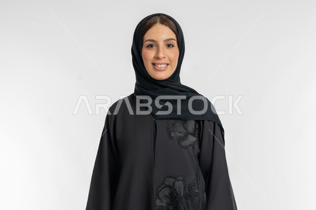 مفهوم الموضة والأناقة, الاهتمام والعناية بالمظهر الخارجي, بورتريه مقرب لامرأة عربية خليجية إماراتية ترتدي الحجاب والعباءة السوداء تقف بتعابيرالنعومة والانوثة, شابة سعودية تنظر إلى الكاميرا بإيماءات السعادة والسرور, خلفية بيضاء