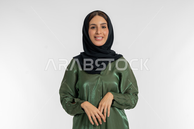 مفهوم الموضة والأناقة, الاهتمام والعناية بالمظهر الخارجي, بورتريه مقرب لامرأة عربية خليجية إماراتية ترتدي الحجاب تقف بتعابيرالحياء والخجل, شابة سعودية تنظر إلى الكاميرا بإيماءات السعادة والسرور, خلفية بيضاء