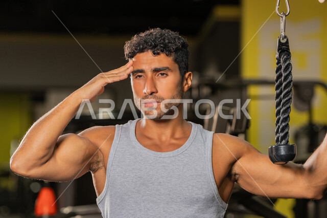بناء الكتلة العضلية للجسم، رجل سعودي يستعد لممارسة أنشطة لتقوية العضلات، الاهتمام بالصحة واللياقة الجسدية، صورة مقربة لشاب عربي خليجي إماراتي يرتدي الزي الرياضي يضع يده على رأسه ينظر إلى شيء ما بإيماءات القوة والثقة، رياضة كمال الأجسام، اتباع أسلوب حياة صحي