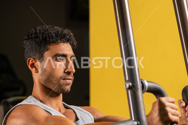 Burning fat and losing weight, close-up of a young Arab Gulf Emirati man in sportswear doing weight lifting exercises, using sports equipment, healthy lifestyle, Saudi man doing muscle strengthening activities, gestures of strength and confidence, interest in health and fitness, bodybuilding