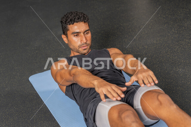 رجل سعودي يمارس أنشطة لتقوية العضلات، شاب عربي خليجي إماراتي يرتدي الملابس الرياضية يقوم بممارسة تمارين الإحماء، حرق الدهون وتقليل الوزن، إيماءات القوة والثقة، مفهوم المحافظة على أسلوب حياة صحي، نشاط بدني للحفاظ على الصحة واللياقة الجسدية