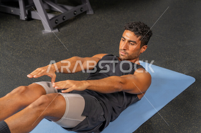 إيماءات القوة والثقة، مفهوم المحافظة على أسلوب حياة صحي، حرق الدهون وتقليل الوزن، رجل سعودي يمارس أنشطة لتقوية العضلات، شاب عربي خليجي إماراتي يرتدي الملابس الرياضية يقوم بممارسة تمارين الإحماء، نشاط بدني للحفاظ على الصحة واللياقة الجسدية