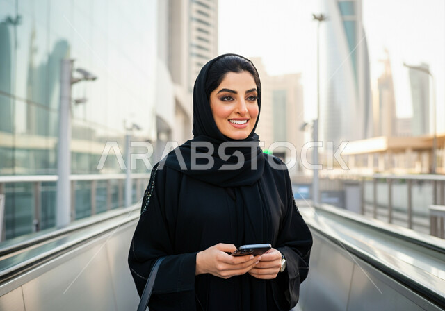 تيسير الحركه المروريه للشعب السعودي, إستخدام الهاتف المحمول, إمرأه عربيه سعوديه خليجيه مبتسمه  ترتدي الحجاب و العباءه السوداء تقف في محطة قطار الرياض,  إيماءات السعاده والرضا بالخدمات الحديثه ,تقدم وسائل المواصلات  في المملكه , التنقل السريع والآمن عبر الميترو في السعوديه