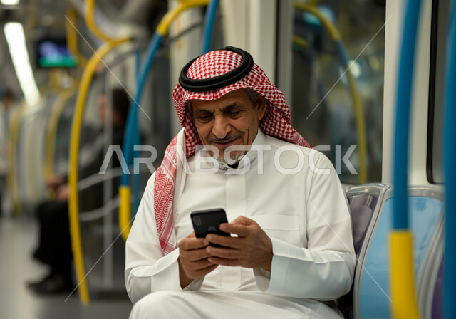 تطور وسائل النقل والمواصلات في المملكة, رجل عربي خليجي سعودي يرتدي الثوب التقليدي والشماغ يجلس داخل مترو الرياض ويستعمل الهاتف المحمول, استخدام الأجهزة التقنية الحديثة, توفير خدمات التنقل السريع والآمن