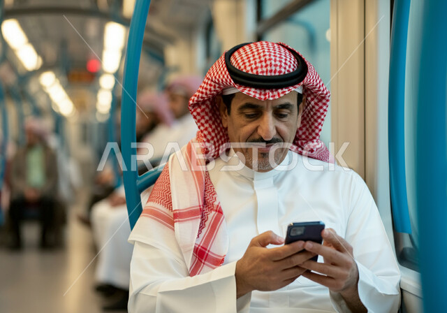 تطور وسائل النقل والمواصلات في المملكة, توفير خدمات التنقل السريع والآمن, صورة مقربة لرجل عربي خليجي سعودي يرتدي الثوب التقليدي والشماغ يجلس داخل مترو الرياض ويستعمل الهاتف المحمول, استخدام الأجهزة التقنية الحديثة