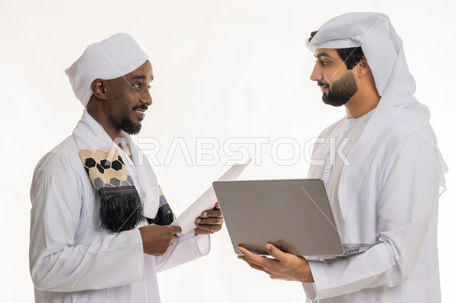 مناقشة الخطط والمشاريع, تبادل الخبرات والمهارات, التعاون في إنجاز مهام العمل, استخدام الأجهزة التقنية الحديثة والمتطورة, بورتريه مقرب لشاب عربي خليجي إماراتي يرتدي الكندورة والغترة البيضاء يعمل مع رجل سوداني, خلفية بيضاء