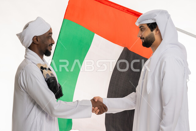 National holidays and occasions, Flag Day commemoration November 3, UAE National Day celebration December 2, Handshake and agreement concept, Close-up portrait of a young Emirati Gulf Arab man wearing a white kandura and ghutra shaking hands with a Sudanese man, white background