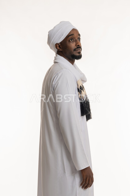 Standing up straight, concept of elegance and masculinity, concern for one's appearance, side portrait of a Sudanese Arab man wearing a Sudanese galabiya and turban looking at something above, white background