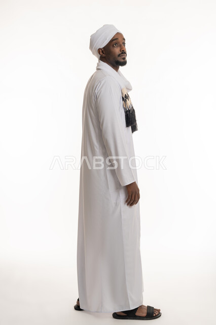 مفهوم الاهتمام بالأناقة والمظهر الخارجي, الوقوف باستقامة واعتدال, بورتريه من الجانب لرجل عربي سوداني يرتدي الجلابية والعمامة السودانية ينظر إلى شيء ما بالأعلى, الجسم بالطول الكامل, خلفية بيضاء