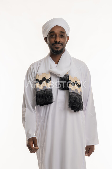 الوقوف باستقامة واعتدال, مفهوم الأناقة والرجولة, الاهتمام بالمظهر الخارجي, بورتريه لرجل عربي سوداني مبتسم يرتدي الجلابية والعمامة السودانية ينظر إلى الكاميرا بإيماءات السعادة والسرور, خلفية بيضاء