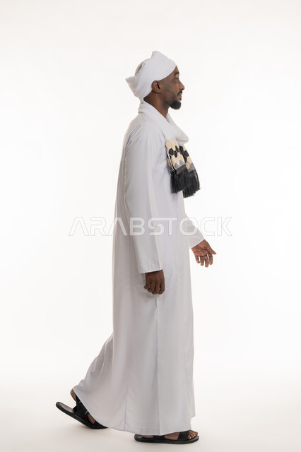 Going somewhere, concept of elegance and masculinity, concern for appearance, side portrait of smiling Sudanese Arab man wearing Sudanese galabiya and turban walking, full body, white background