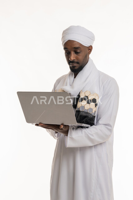 إنجاز مهام العمل عن بعد, استخدام الأجهزة التقنية الحديثة والمتطورة, بورتريه لرجل عربي سوداني يرتدي الجلابية والعمامة السودانية يقوم باستعمال جهاز الحاسوب المحمول, خلفية بيضاء