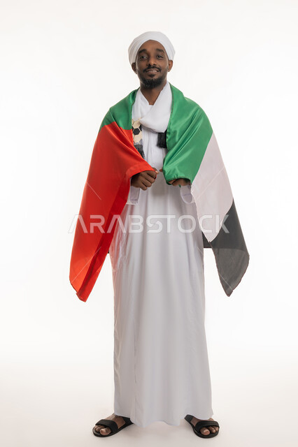 تعابير الحب والانتماء, الاحتفال بالأعياد والمناسبات الوطنية, اليوم الوطني الإماراتي 2 ديسمبر, استذكار يوم العلم 3 نوفمبر, بورتريه لرجل عربي سوداني يرتدي الجلابية والعمامة السودانية يضع علم الإمارات على ظهره, الجسم بالطول الكامل, خلفية بيضاء