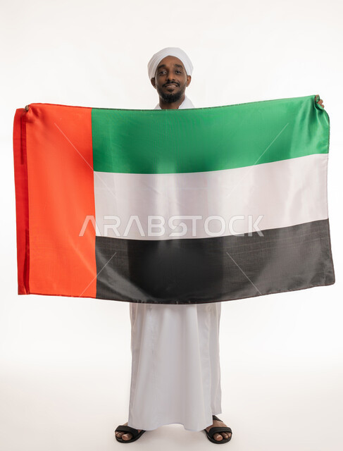 Celebrating national holidays and occasions, concept of love and belonging, UAE National Day December 2, Commemorating Flag Day November 3, Portrait of a smiling Sudanese Arab man wearing a Sudanese jalabiya and turban holding the flag of the United Arab Emirates, full body, white background