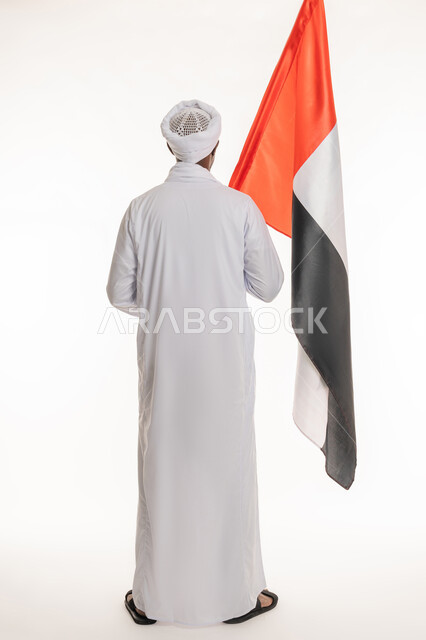 اليوم الوطني الإماراتي 2 ديسمبر, الاحتفال بالأعياد والمناسبات الوطنية, استذكار يوم العلم 3 نوفمبر, بورتريه من الخلف لرجل عربي سوداني يرتدي الجلابية والعمامة السودانية يحمل علم الإمارات العربية المتحدة, الجسم بالطول الكامل, خلفية بيضاء