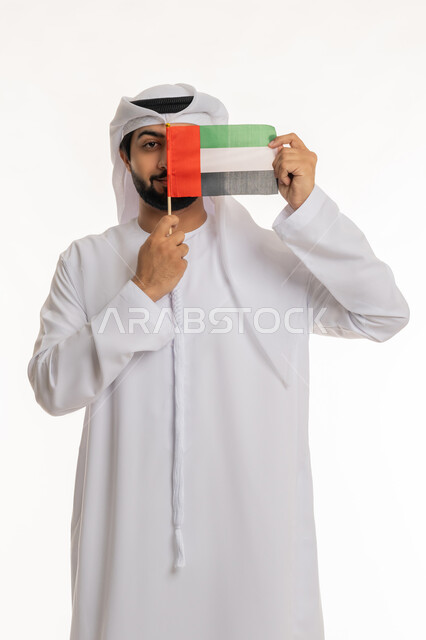Celebrating national holidays and occasions, the concept of love and pride in the homeland, expressions of belonging and pride in the Emirati identity, the memory of the UAE National Day, December 2, portrait of an Arab Gulf Emirati man wearing a white kandura and ghutra holding the UAE flag, white background