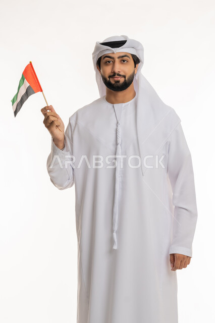 تعابير الانتماء والاعتزاز بالهوية الإماراتية, الاحتفال بالأعياد والمناسبات الوطنية, مفهوم الحب والفخر بالوطن, ذكرى اليوم الوطني الإماراتي 2 ديسمبر, بورتريه لرجل عربي خليجي إماراتي يرتدي الكندورة والغترة البيضاء يحمل بيده علم الإمارات، خلفية بيضاء