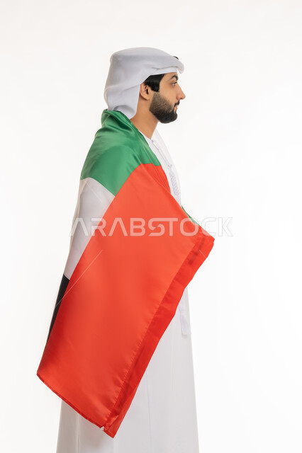 الاحتفال بالأعياد والمناسبات الوطنية, مفهوم الحب والفخر بالوطن, تعابير الانتماء والاعتزاز  بالهوية الإماراتية, ذكرى اليوم الوطني الإماراتي 2 ديسمبر, بورتريه من الجانب لرجل عربي خليجي إماراتي يرتدي الكندورة والغترة البيضاء يضع علم الإمارات على ظهره، خلفية بيضاء
