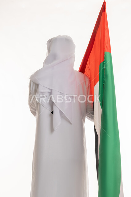 الاحتفال بالأعياد والمناسبات الوطنية, مفهوم الحب والفخر بالوطن, الانتماء والاعتزاز بالهوية الإماراتية, ذكرى اليوم الوطني الإماراتي 2 ديسمبر, بورتريه من الخلف لرجل عربي خليجي إماراتي يرتدي الكندورة والغترة البيضاء يحمل علم الإمارات، خلفية بيضاء