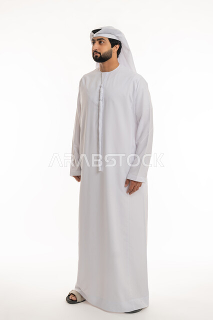 الوقوف باستقامة واعتدال, مفهوم الرجولة والأناقة, الاهتمام بالمظهر الخارجي, بورتريه لرجل عربي خليجي إماراتي يرتدي الكندورة والغترة البيضاء ينظر إلى شيء ما, الجسم بالطول الكامل, خلفية بيضاء