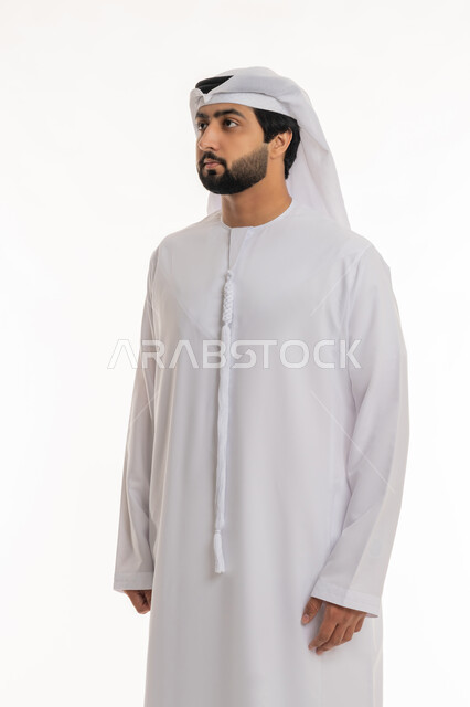 مفهوم الرجولة والأناقة, الاهتمام بالمظهر الخارجي, الوقوف باستقامة واعتدال, بورتريه لرجل عربي خليجي إماراتي يرتدي الكندورة والغترة البيضاء ينظر إلى شيء ما, خلفية بيضاء