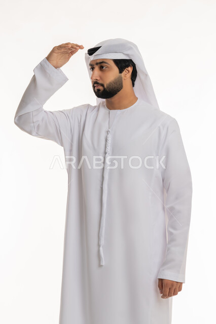تعابير محاولة رؤية الأشياء البعيدة, مفهوم التطلع للمستقبل, النظر لمكان ما, بورتريه لرجل عربي خليجي إماراتي يرتدي الكندورة الغترة البيضاء يرفع يده إلى رأسه بإيماءات البحث عن شيء محدد, خلفية بيضاء