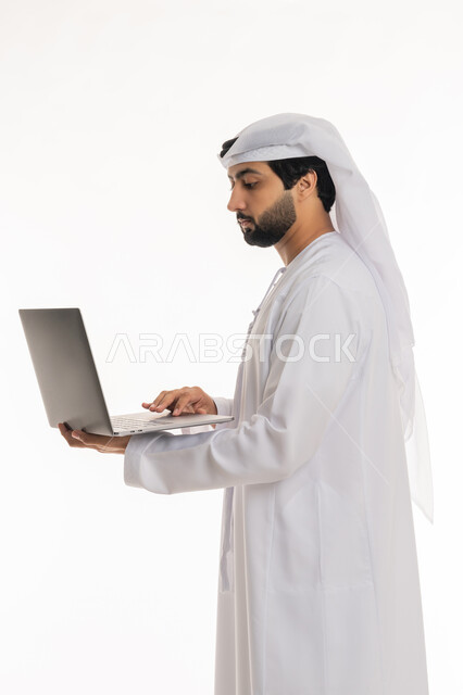 إيماءات التركيز في شاشة الكمبيوتر, استخدام الأجهزة التقنية الحديثة والمتطورة لإنجاز المهام والمشاريع, تصفح مواقع التواصل الاجتماعي والعمل عن بعد, بورتريه لرجل عربي خليجي إماراتي يرتدي الكندورة والغترة البيضاء يعمل على الحاسوب المحمول, خلفية بيضاء