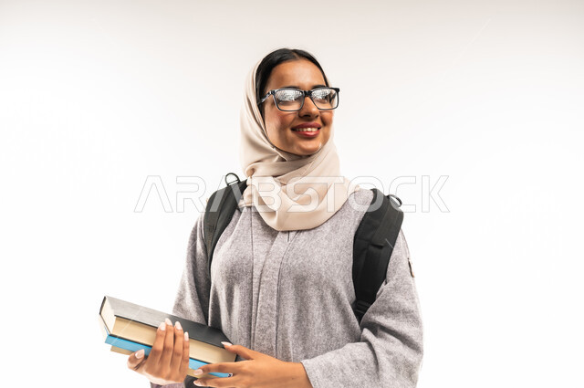 Universities and educational schools, preparing for the new academic year, close-up portrait of an Arab Gulf Omani female university student carrying a university bag and holding a group of books in her hand, a diligent young Saudi woman eager to go to university, white background.