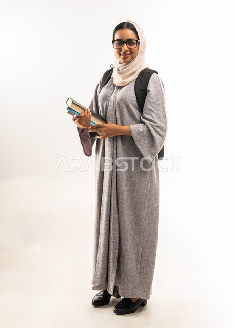 الاستعداد للعام الدراسي الجامعي الجديد, شابة سعودية مجتهدة متشوقة للذهاب الى الجامعه, مدارس وجامعات تعليمية، بورتريه لطالبة جامعية عربية خليجية عمانية  تحمل الحقيبة الجامعية تمسك بيدها مجموعة من الكتب, الجسم بالطول الكامل، خلفية بيضاء