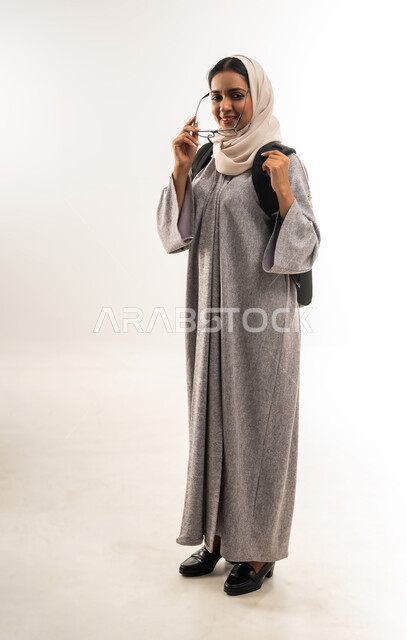 الاستعداد للعام الدراسي الجامعي الجديد, بورتريه طالبة جامعية عربية خليجية عمانية  تحمل الحقيبة الجامعية تمسك بيدها النظارة,  شابة سعودية مجتهدة متشوقة للذهاب الى الجامعه, مدارس وجامعات تعليمية,  الجسم بالطول الكامل، خلفية بيضاء .