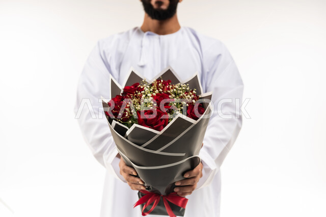 انتقاء باقة مميزة من الورود، تقديم الزهور في الأعياد والمناسبات السعيدة، بورتريه مقرب لرجل عربي خليجي عماني يرتدي الدشداشة و الكمة يحمل بيده باقة من الورد الاحمر، خلفية بيضاء